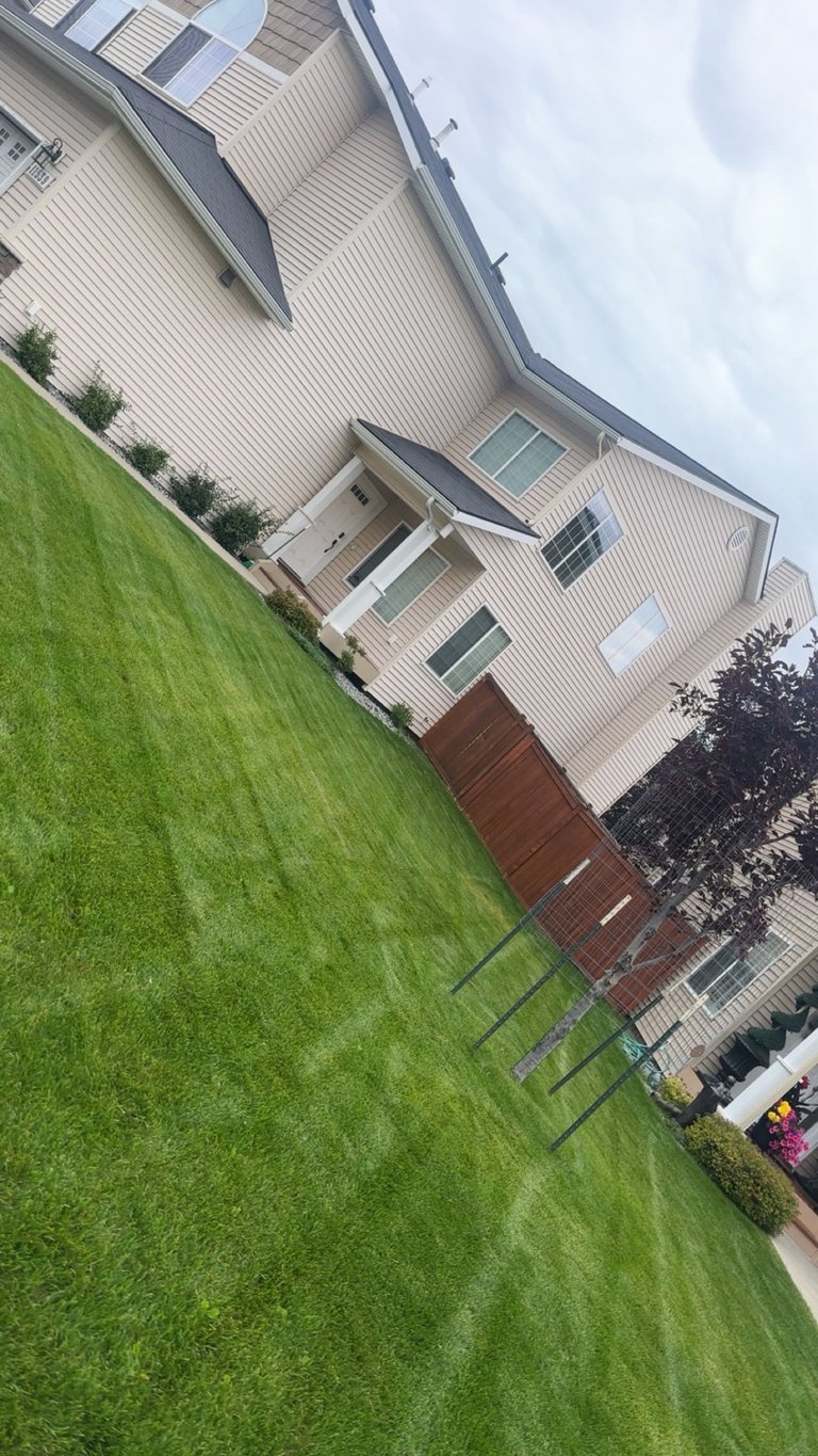 Aerial view of a suburban home with white and dark gray siding, sloped roof, surrounded by manicured green lawn and landscaping